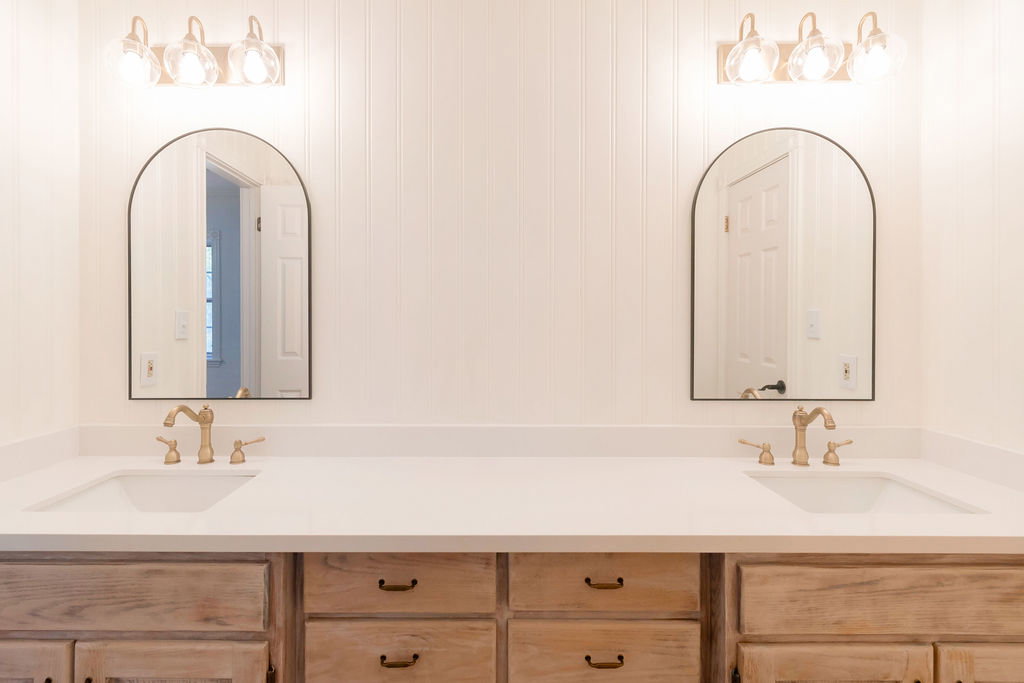 Dual vanity with integrated sinks, light wood-finish cabinetry, and brushed gold hardware