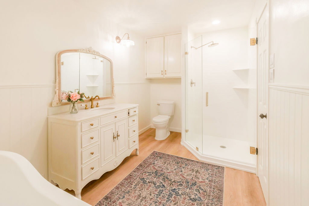 Light-toned bathroom featuring a detailed vanity with an ornate mirror, a glass-enclosed shower with subway tile, built-in cabinetry, and wood-finish flooring