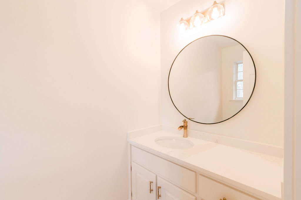 Bathroom vanity featuring a polished gold single-handle faucet, a circular mirror with a black frame, and a four-light fixture