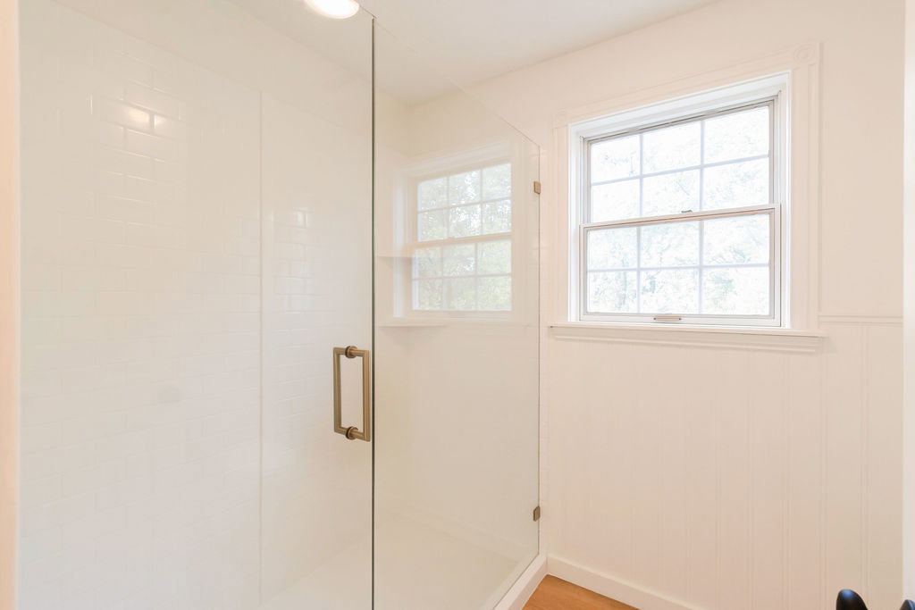 Glass-enclosed shower with white subway tile surround and a brushed bronze handle