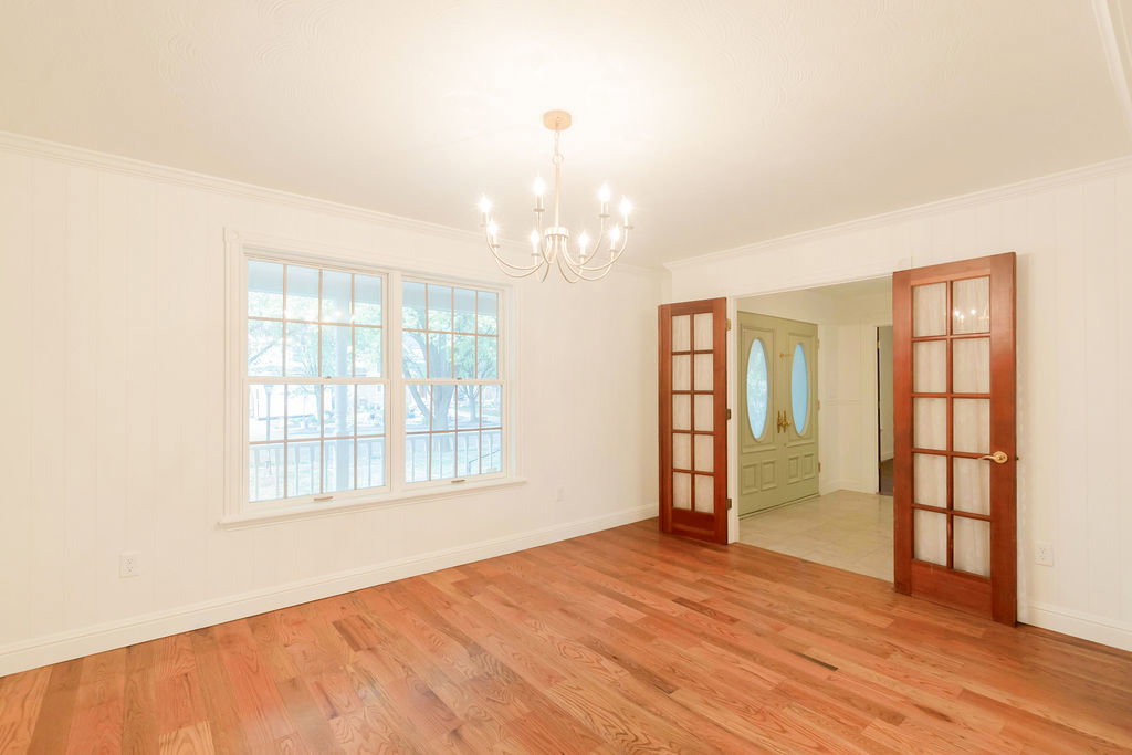 Hardwood flooring throughout featuring white vertical wall paneling, a chandelier light fixture, and crown molding