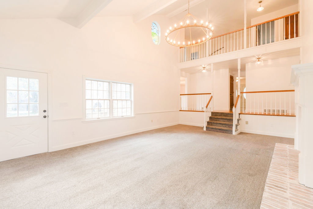 Vaulted ceiling living space with a second-story overlook, featuring a decorative chandelier, a brick hearth, and multi-pane windows
