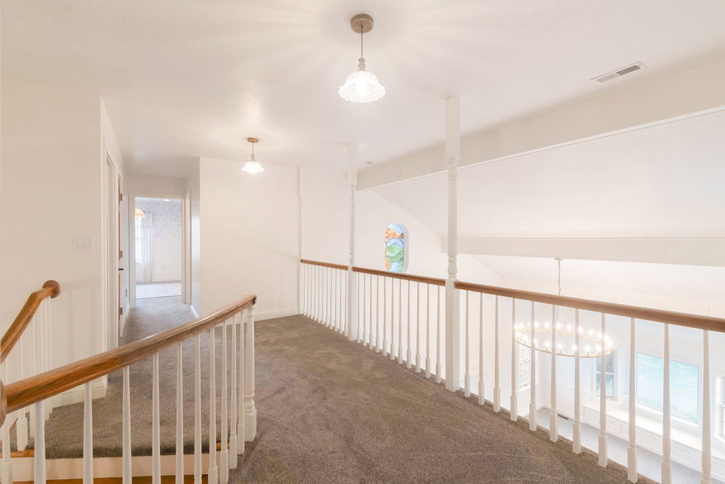Upper-level hallway with gray carpet, white walls, and a white balustrade with wood handrails