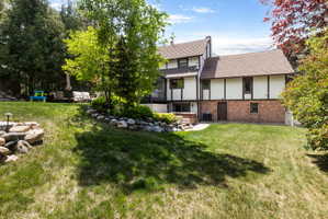 Expansive terraced backyard featuring a stone-lined garden bed, mature trees, and a paved patio area