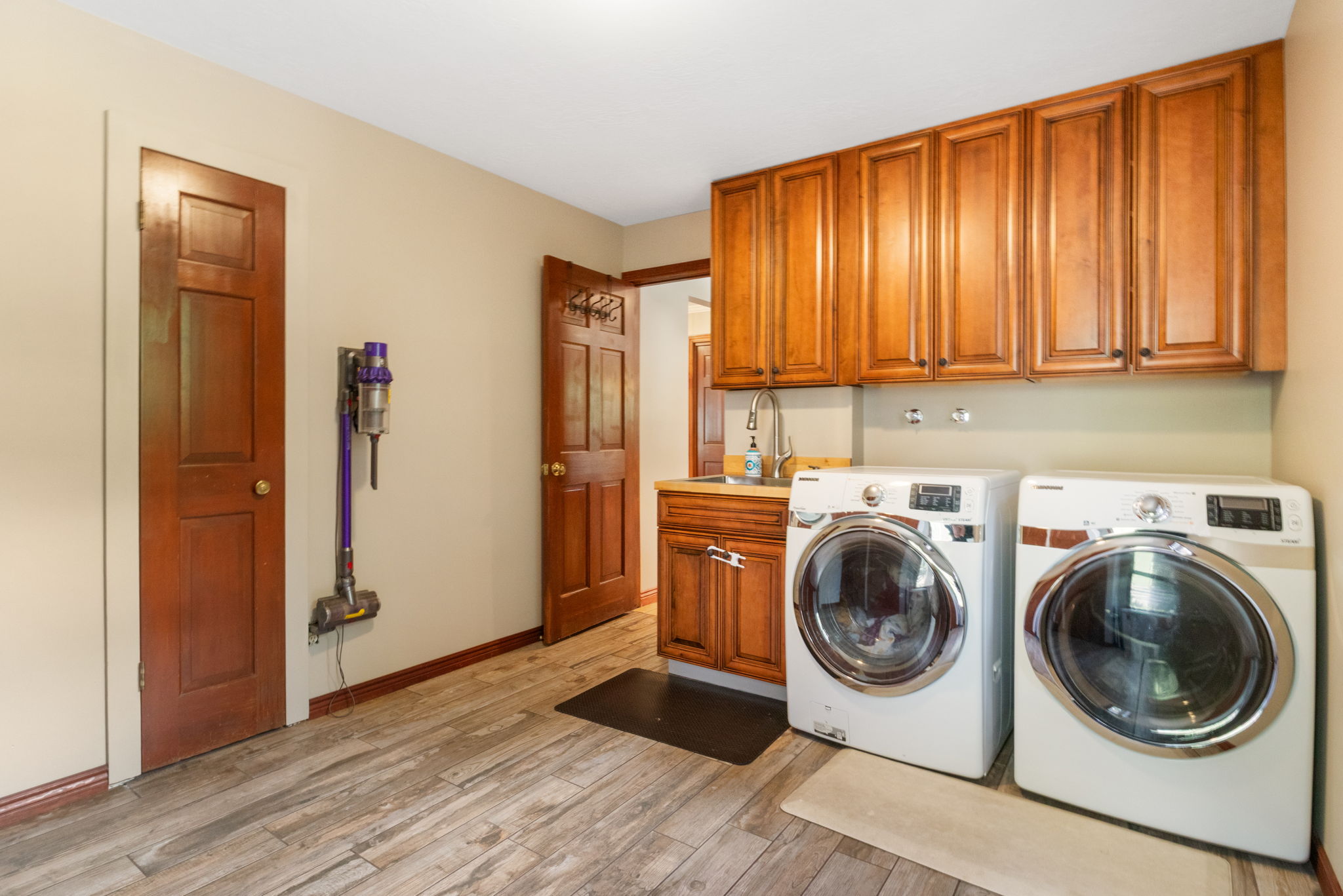 Laundry room featuring wood-finish flooring, built-in cabinetry, a utility sink with a chrome faucet, and a light neutral wall color