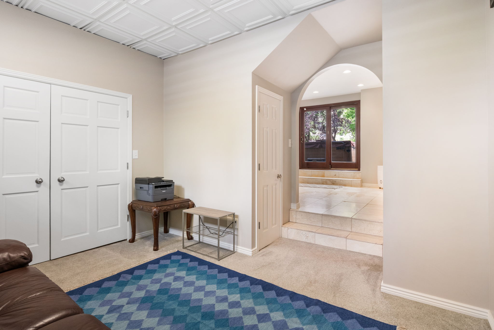 Recessed lighting illuminates an arched entryway leading to a tile-floored area with brown-framed sliding glass doors