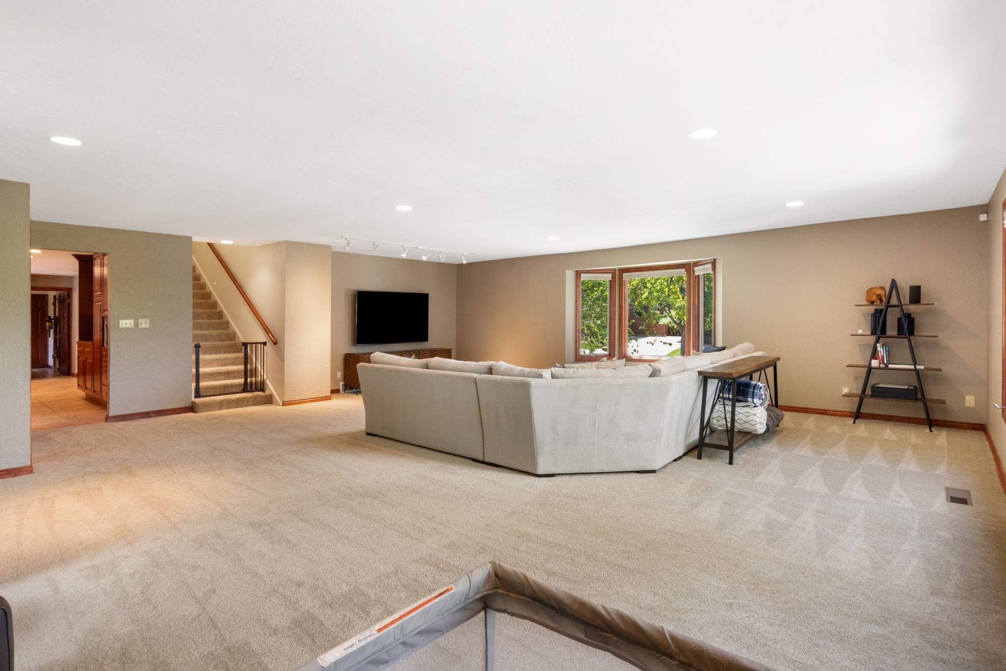 Spacious carpeted living area featuring recessed lighting, a bay window with wood-finish trim, a staircase with wood handrails and metal balusters, and an arched doorway
