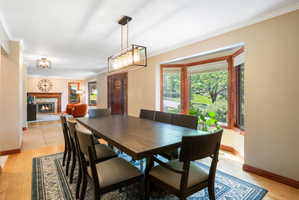 Dining area featuring wood-finish flooring, a rectangular chandelier with a dark metal frame, and a wide bay window with wood trim