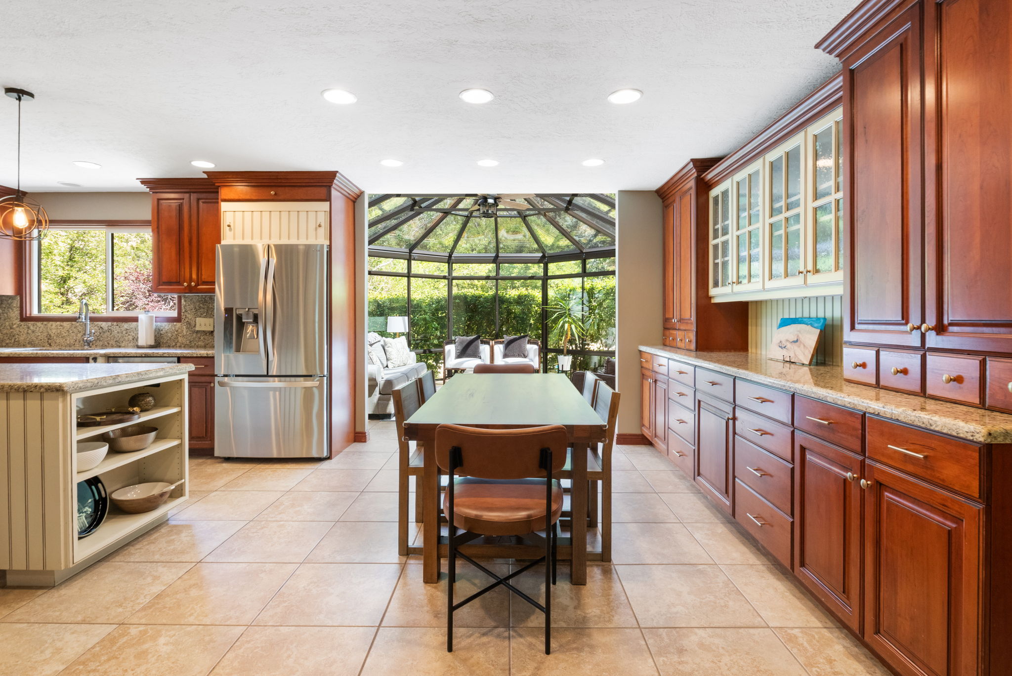 Kitchen featuring warm wood cabinetry, light-toned tile flooring, recessed ceiling lighting, a built-in stainless steel refrigerator, and granite countertops