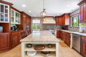 Kitchen featuring an expansive island with a light-colored countertop, rich wood cabinetry, stainless steel appliances, and a built-in range hood