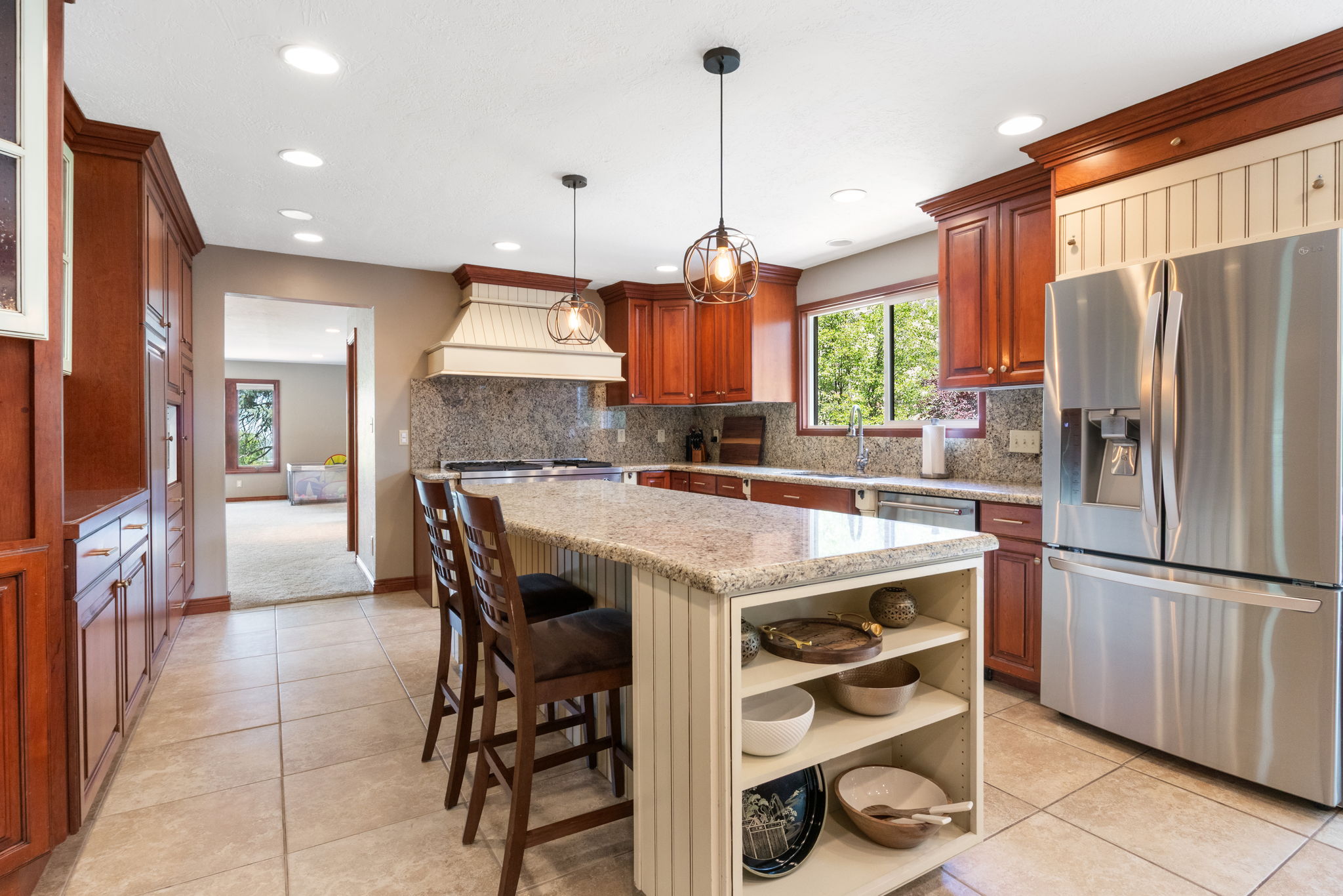 Kitchen featuring a central island with integrated shelving, granite countertops, tile flooring, rich wood cabinetry, and stainless steel appliances