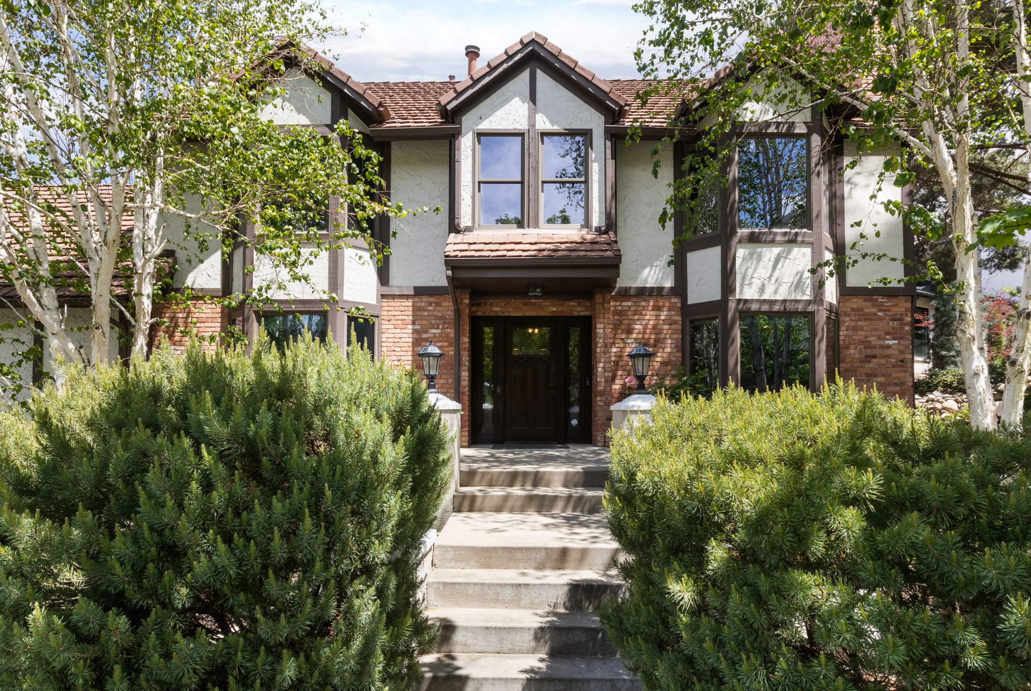 Tudor-style facade featuring brick and stucco accents, multi-pane windows, and a prominent dark wood entry door
