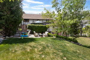 Spacious backyard featuring a manicured lawn, stone retaining walls, mature trees, and a paved patio area