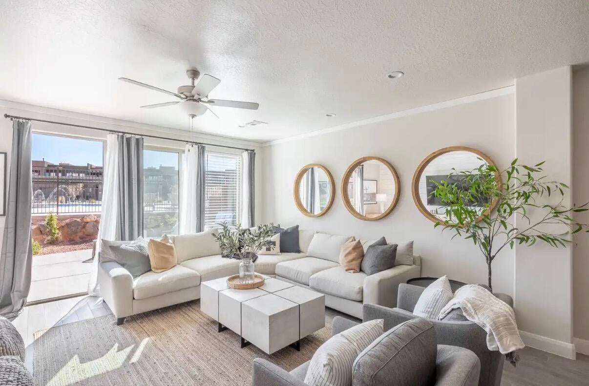 Spacious living area featuring large sliding glass doors, multiple windows with blinds, a ceiling fan, crown molding, and recessed lighting