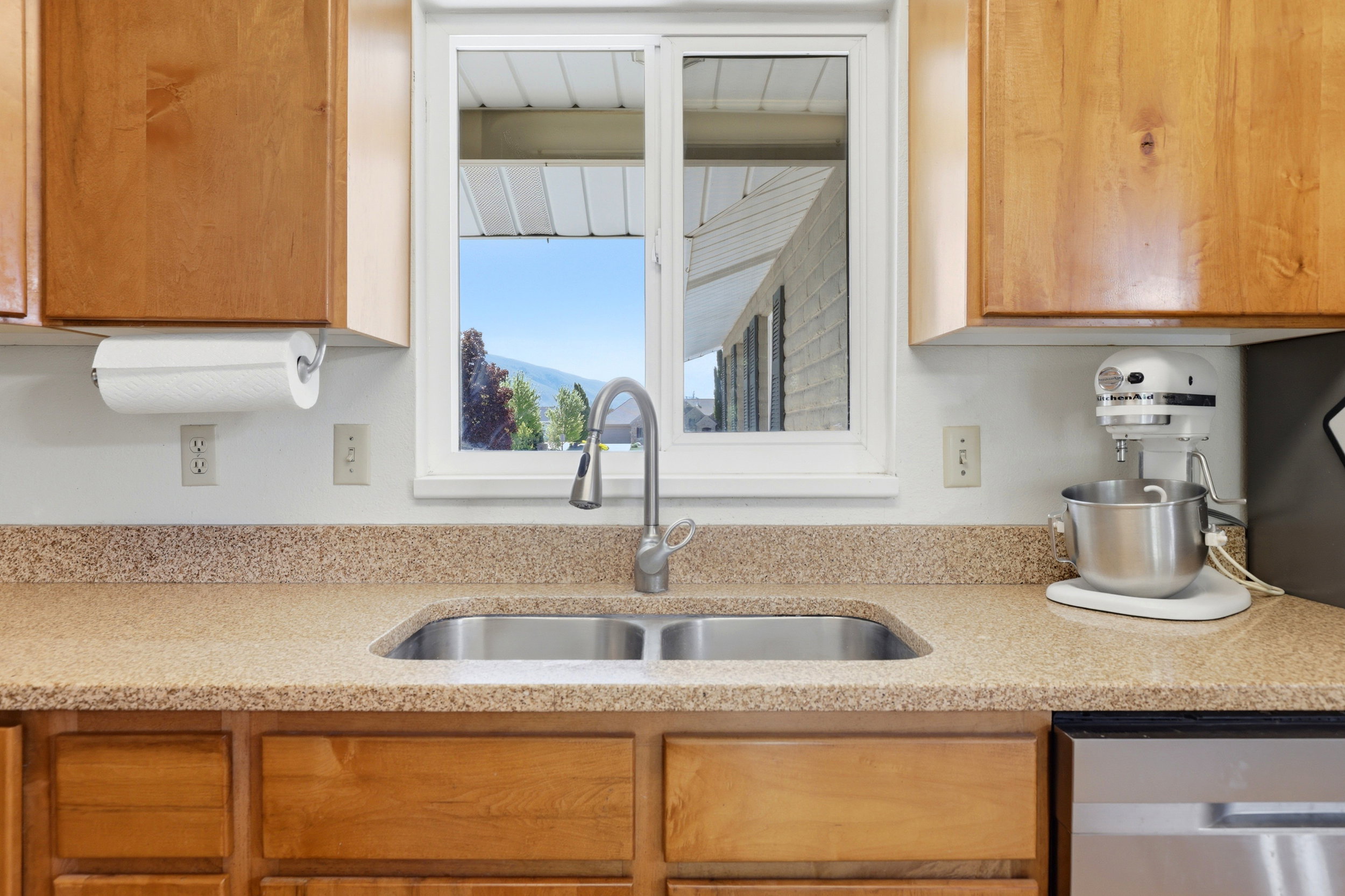 Kitchen sink area featuring a dual basin stainless steel sink, a chrome gooseneck faucet, and light wood-finish cabinetry