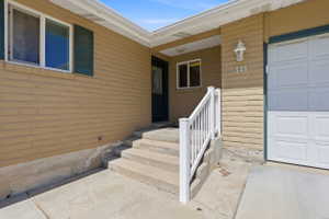 Front exterior featuring tan brick siding, white window trim, dark green shutters, a white garage door, and concrete steps with a white railing