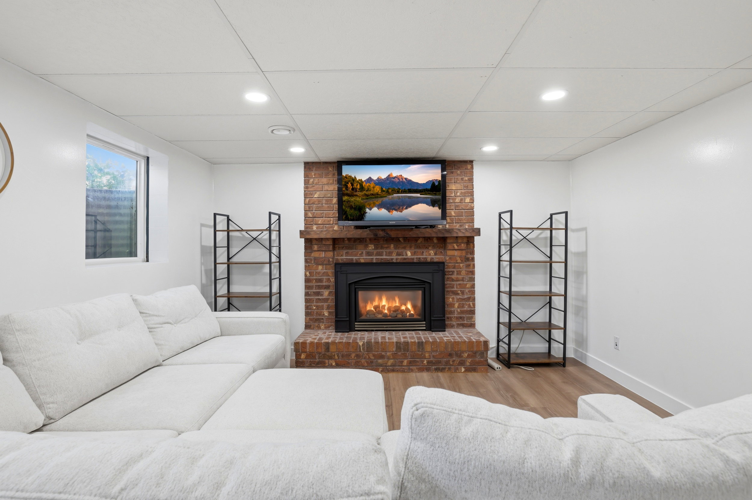 Living area featuring a brick fireplace, built-in shelving, wood-finish flooring, recessed lighting, and a drop ceiling