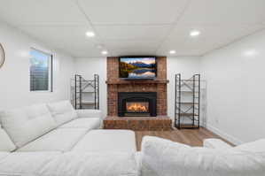 Living area featuring a brick fireplace, built-in shelving, wood-finish flooring, recessed lighting, and a drop ceiling
