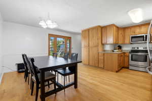 Open-concept kitchen and dining area featuring light wood-finish flooring, natural wood cabinetry, stainless steel appliances, and a wood-frame patio door