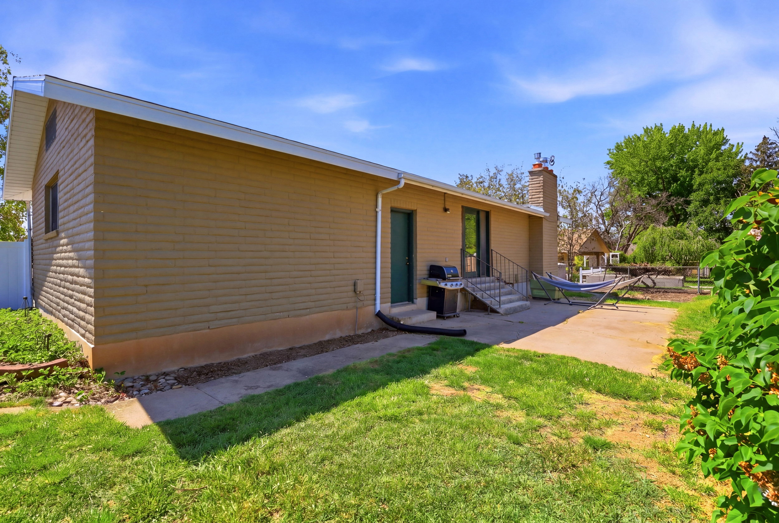 Spacious backyard featuring a concrete patio, a concrete path, a verdant lawn, mature trees, and established shrubbery