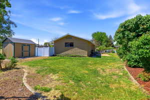 Expansive backyard featuring a green lawn, a detached storage shed with a shingle roof, a white vinyl fence, and mature perimeter landscaping