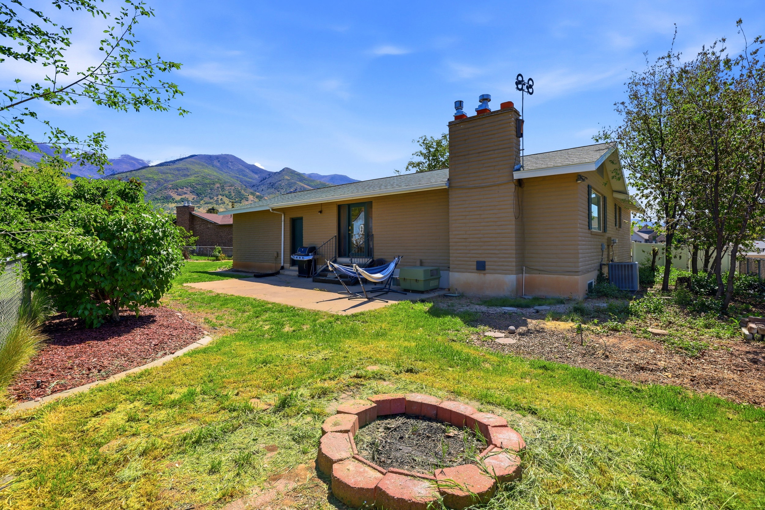 Expansive backyard featuring a concrete patio, a red brick fire pit, and a backdrop of distant mountains