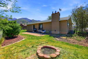 Expansive backyard featuring a concrete patio, a red brick fire pit, and a backdrop of distant mountains