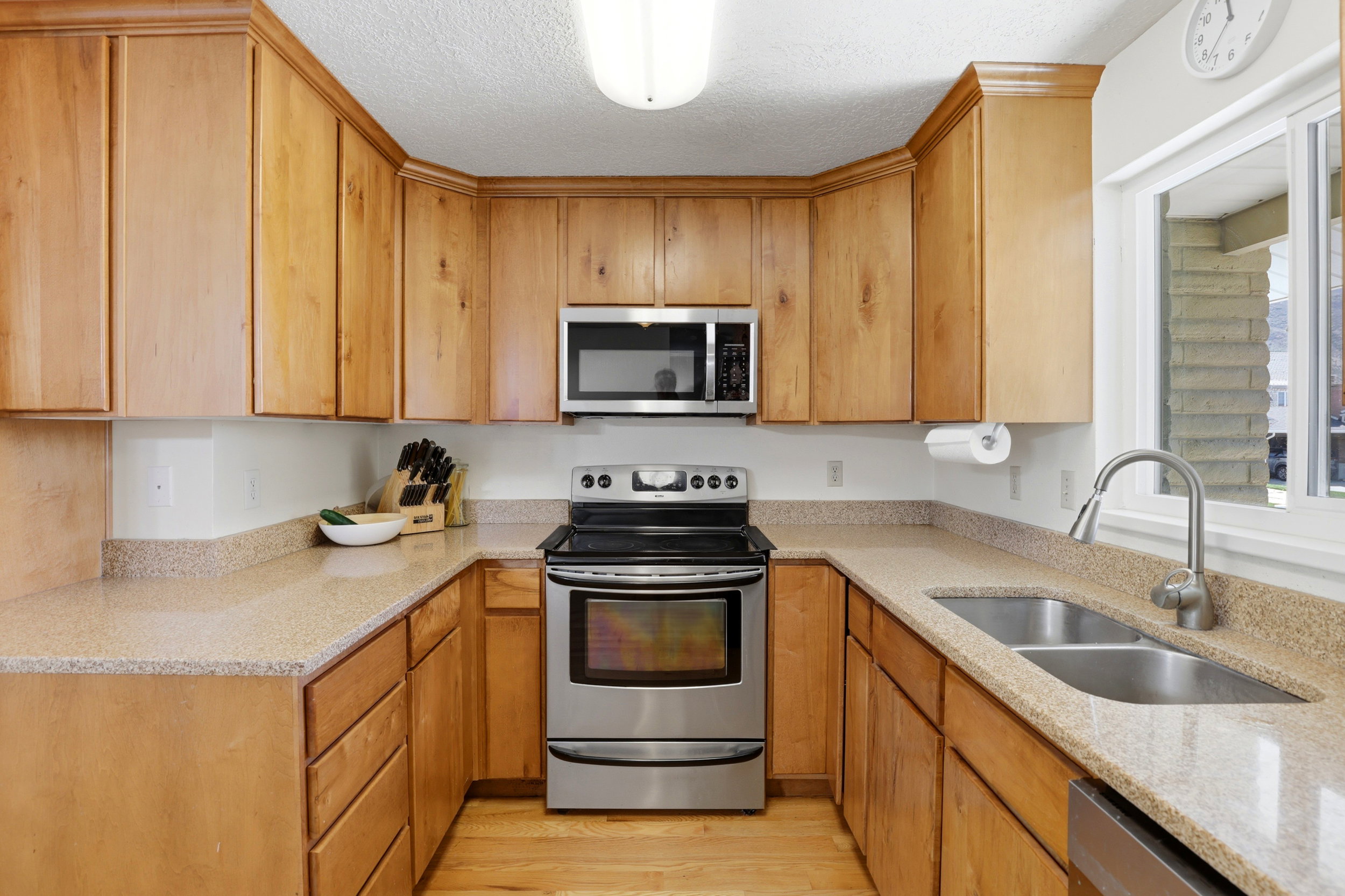 U-shaped kitchen featuring wood cabinetry, speckled countertops, stainless steel appliances, a double basin sink, and a window above the sink