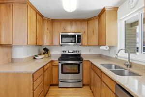 U-shaped kitchen featuring wood cabinetry, speckled countertops, stainless steel appliances, a double basin sink, and a window above the sink