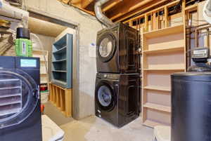 Laundry area featuring a stacked washer and dryer, exposed ceiling joists, and concrete walls