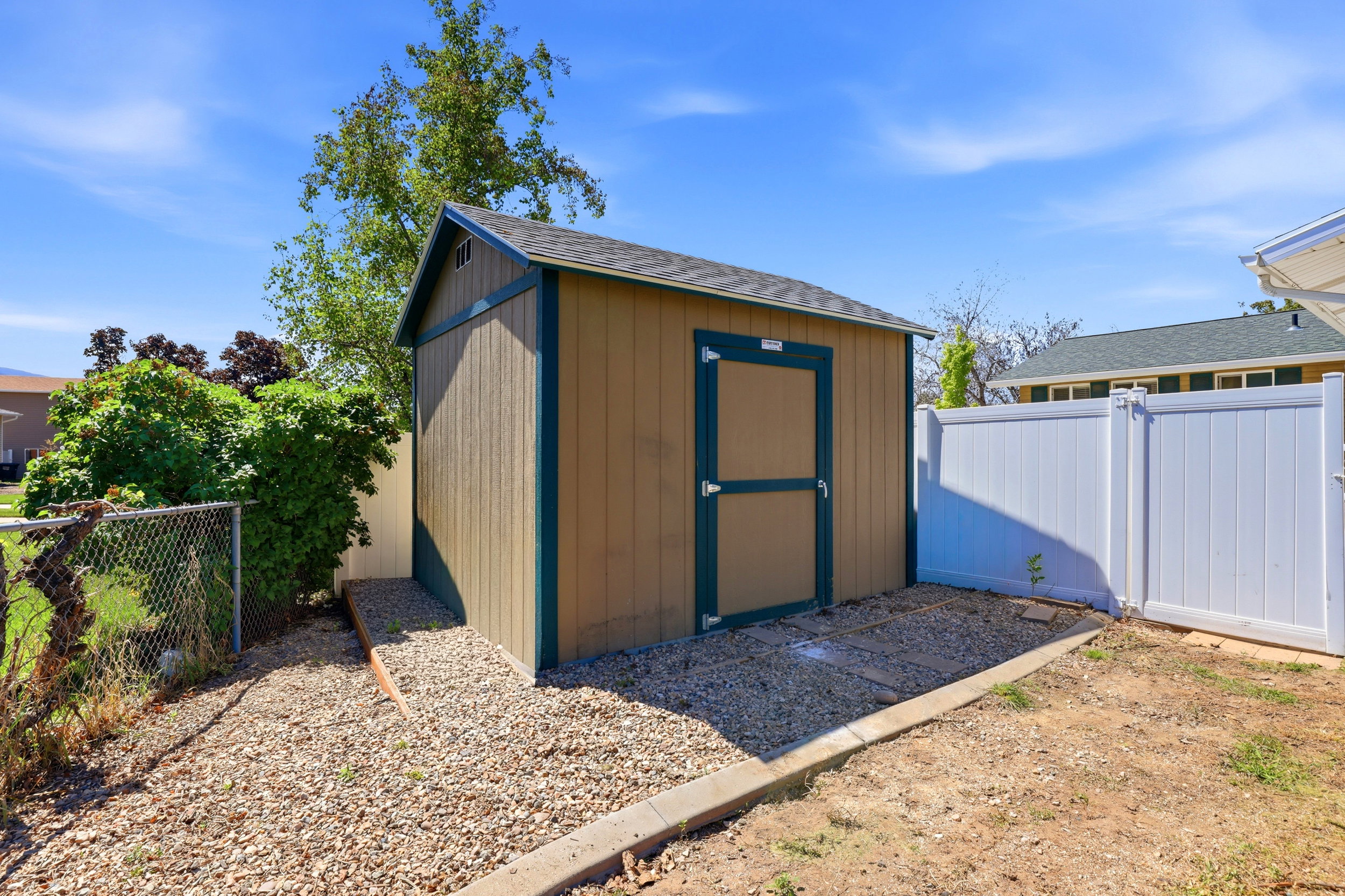 Exterior storage shed featuring a pitched roof, tan siding, and dark trim