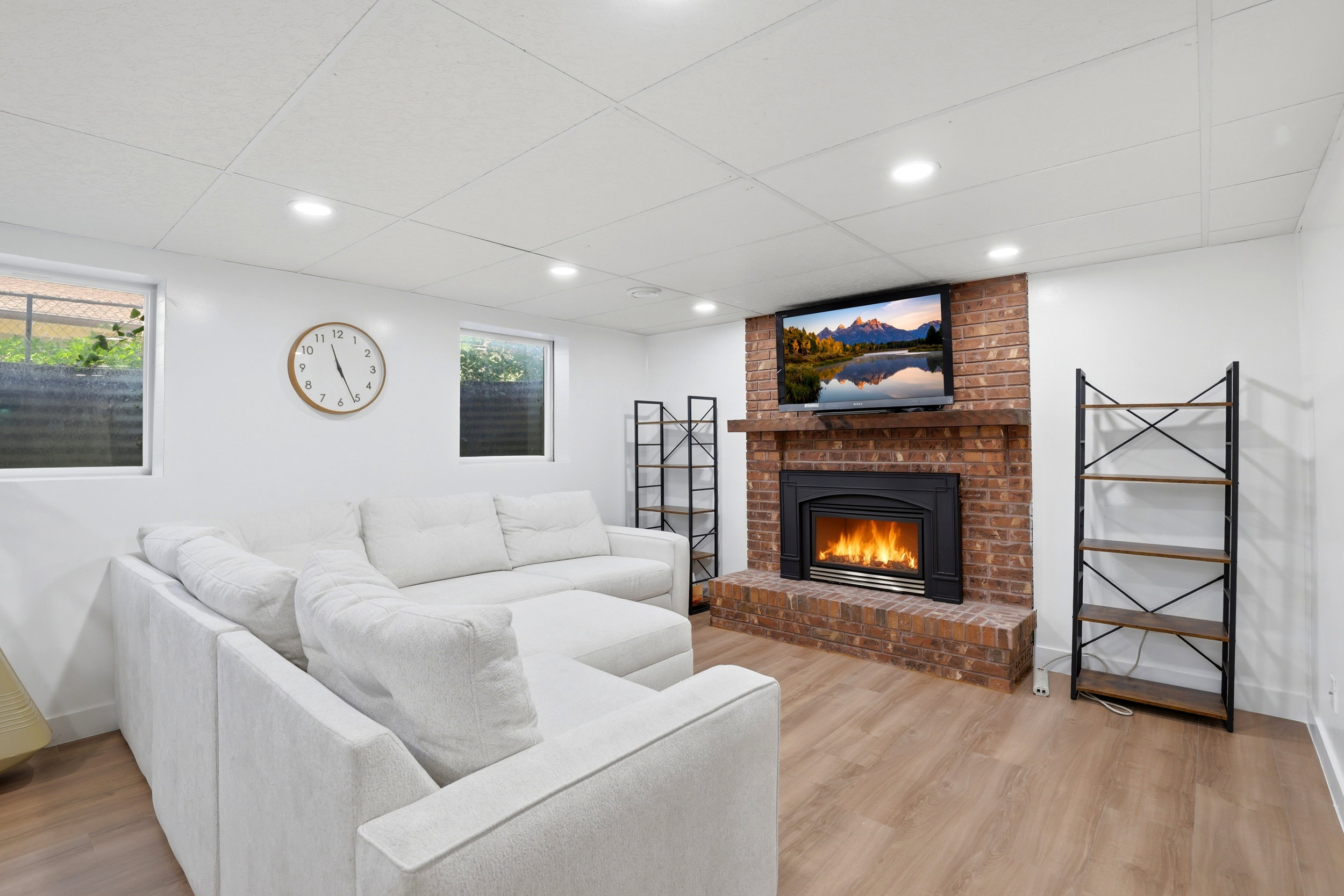 Living area featuring a brick fireplace with a wood mantel, wood-finish flooring, recessed lighting, and white walls