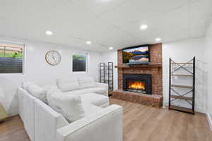 Living area featuring a brick fireplace with a wood mantel, wood-finish flooring, recessed lighting, and white walls