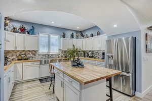 Kitchen featuring an arched entryway, white cabinetry, wood-finish countertops.