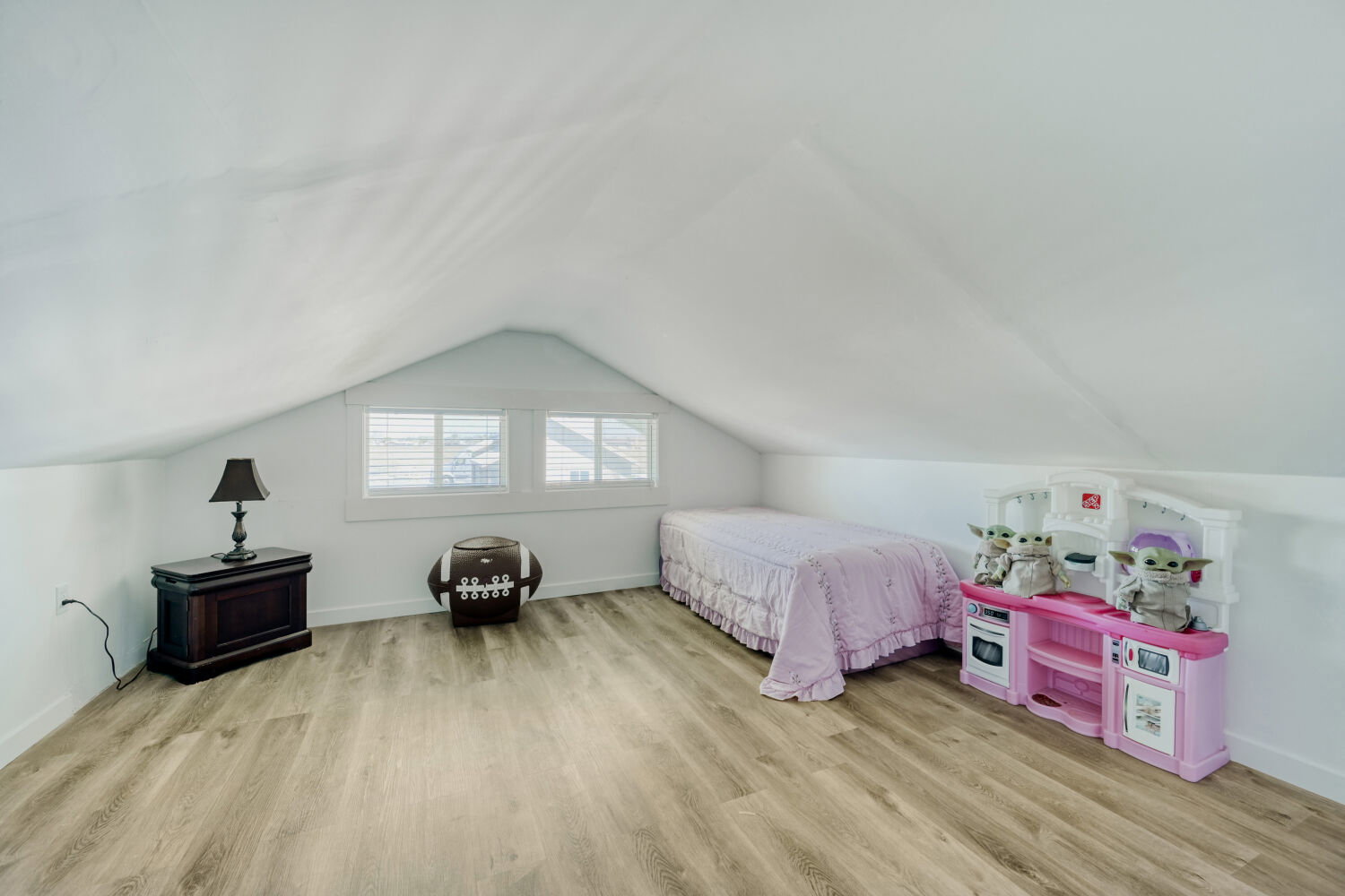 Attic space featuring sloped ceilings, two horizontal windows with blinds, light wood-finish flooring.