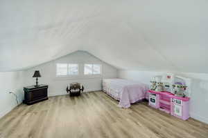 Attic space featuring sloped ceilings, two horizontal windows with blinds, light wood-finish flooring.
