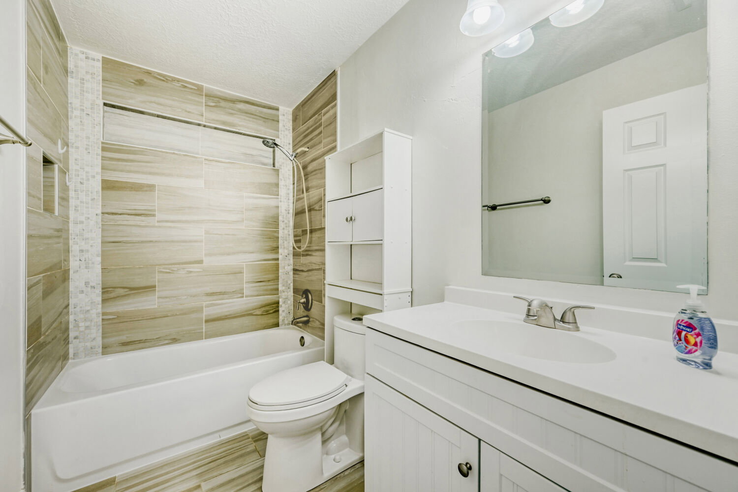 Full bathroom featuring a white porcelain tub, wood-finish tile shower surround, mosaic tile accent, a white vanity with integrated sink, and a large wall-mounted mirror