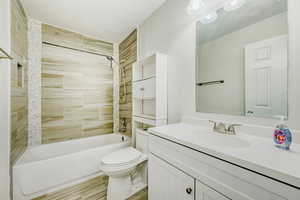 Full bathroom featuring a white porcelain tub, wood-finish tile shower surround, mosaic tile accent, a white vanity with integrated sink, and a large wall-mounted mirror