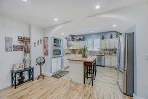 Kitchen featuring a central island with countertop, stainless steel appliances, light-toned cabinetry, and wood-finish flooring