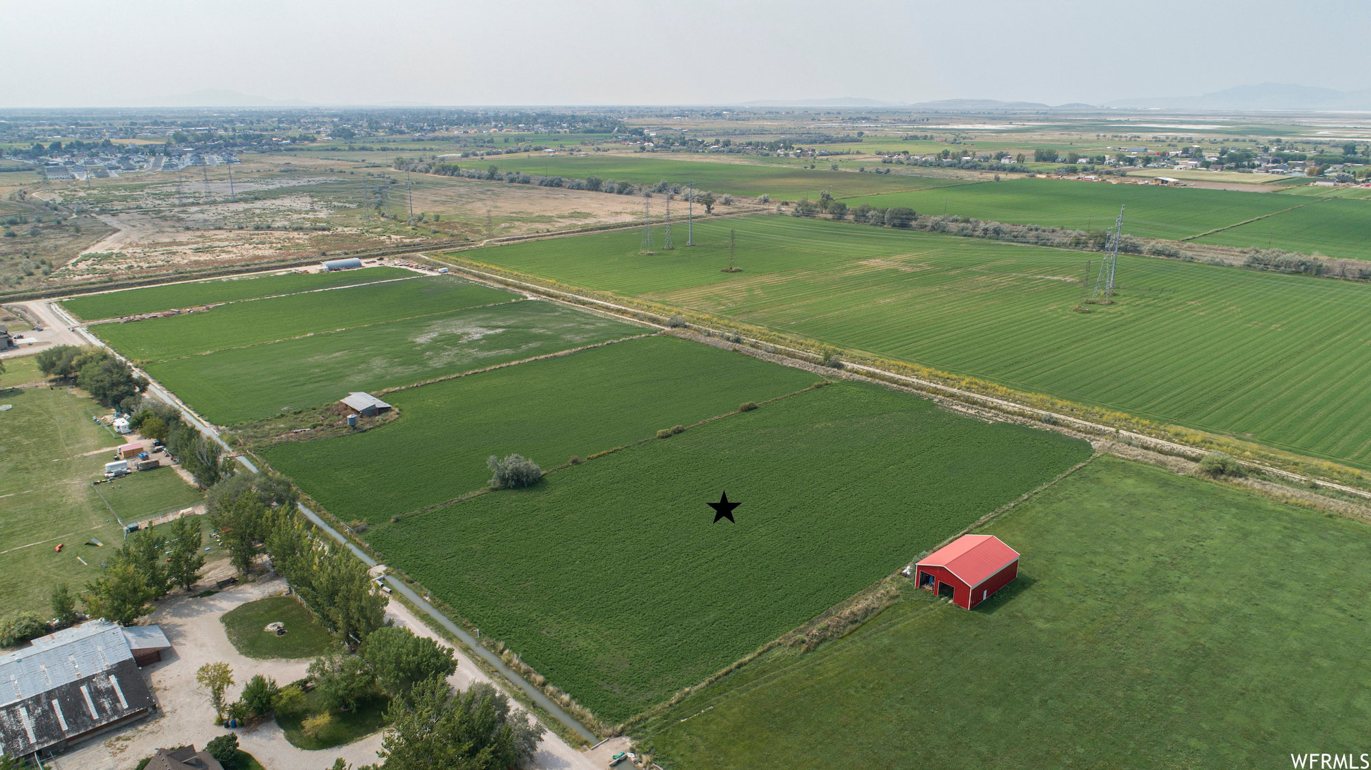 Expansive agricultural land featuring a red barn, a smaller outbuilding, and established trees