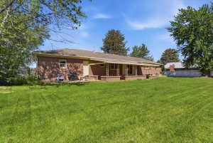 Large green lawn with a brick exterior rambler home featuring a covered patio with columns