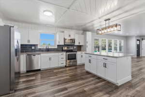 Contemporary kitchen featuring white cabinetry, included stainless steel appliances, a dark subway tile backsplash, granite countertops, and vinyl flooring
