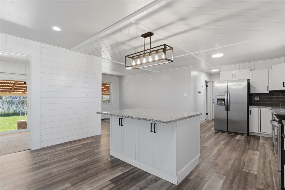 Large kitchen island with a granite countertops, white cabinetry, and matte black hardware