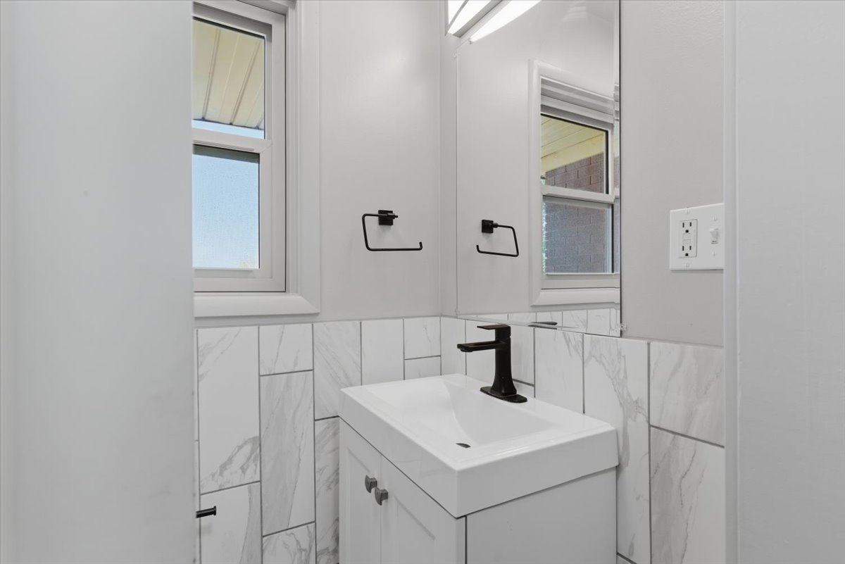 Half bathroom featuring modern vanity with integrated sink, marble-patterned tile, matte black faucet, and white cabinetry