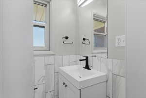 Half bathroom featuring modern vanity with integrated sink, marble-patterned tile, matte black faucet, and white cabinetry