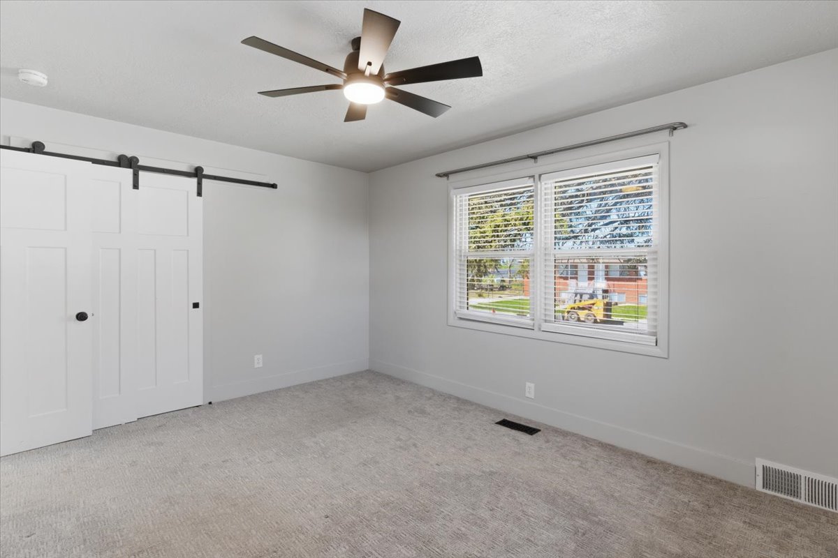 Bedroom featuring a ceiling fan with integrated lighting, large window with blinds, and a built-in barn door closet with black hardware