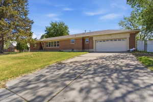 Brick exterior residence featuring a wide concrete driveway, 2 car garage, multiple large windows, and a mature tree providing natural shade