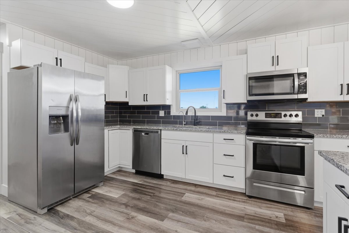 Modern kitchen featuring white cabinetry, granite countertops, and a dark subway tile backsplash