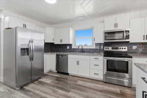 Modern kitchen featuring white cabinetry, granite countertops, and a dark subway tile backsplash
