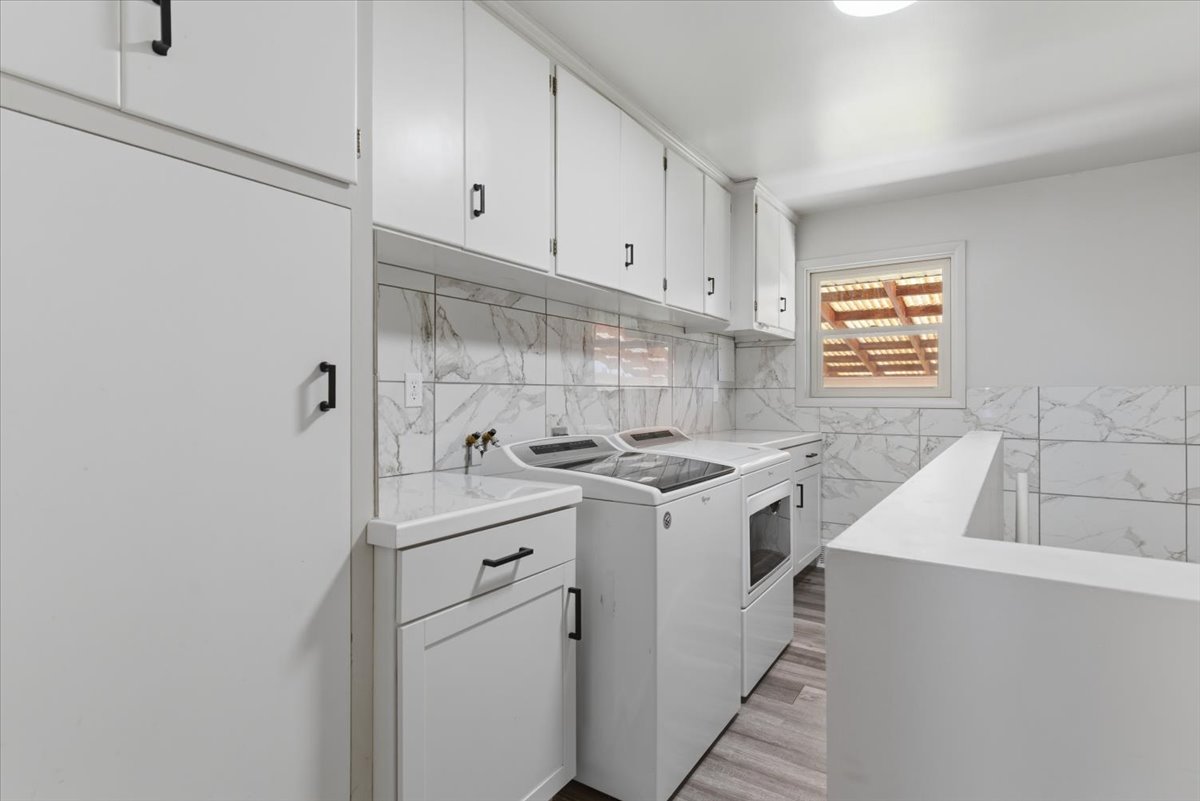 Laundry room featuring white cabinetry, marble-patterned tile backsplash and included washer and dryer.
